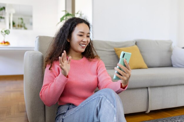 Attractive smiling Asian woman using smart phone while sitting on the sofa at home Communication and video call concept