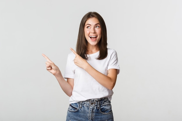 Attractive smiling brunette girl pointing fingers upper left corner, showing logo.