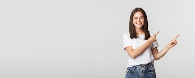 Attractive smiling brunette girl pointing fingers upper right corner showing logo