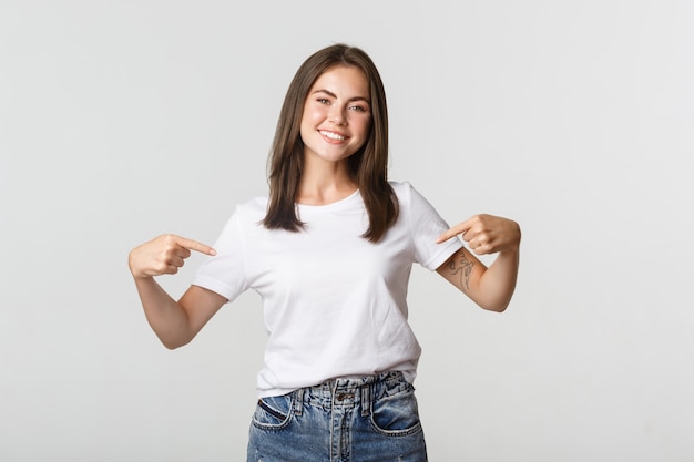 Attractive smiling brunette girl pointing at your logo, showing banner on center.