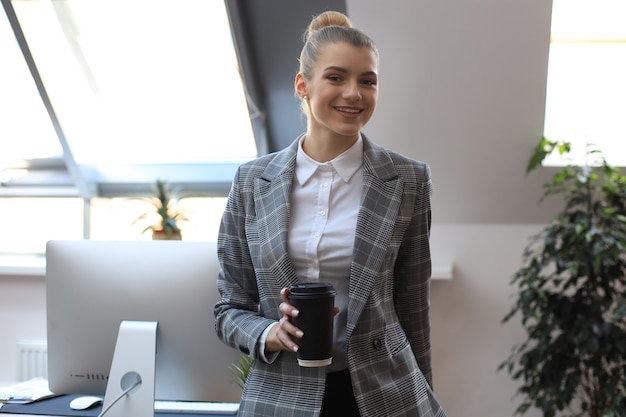 Photo attractive smiling businesswoman standing in the office with a cup of coffee.