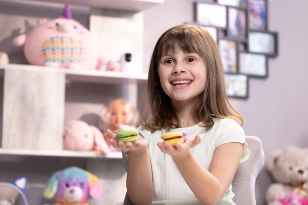 魅力的な笑顔のかわいい学校の子供の女の子は彼女の手で4つのおいしいクッキーを持ってカメラを見てください