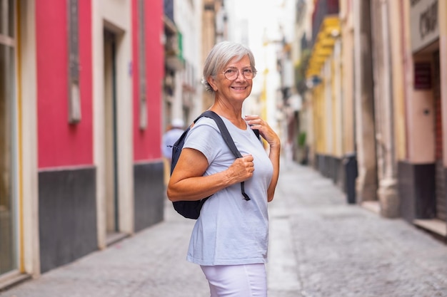 Attractive smiling elderly woman walking in the narrow streets of Seville Spain elderly traveler with backpack visiting the old town