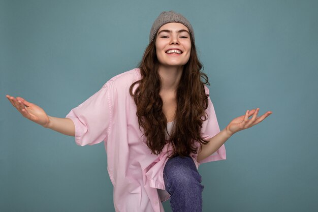 Attractive smiling happy young brunette woman standing isolated over colorful background wall wearing everyday stylish outfit showing facial emotions looking at camera and dancing.