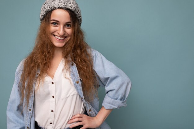 Attractive smiling happy young dark blonde woman standing isolated over colorful background wall wearing everyday stylish outfit showing facial emotions looking at camera