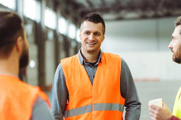 Attractive smiling man foreman wearing workwear talking with colleagues standing in warehouse