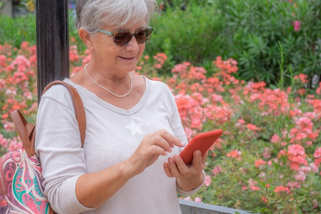 Donna anziana sorridente attraente all'aperto nel parco pubblico mentre si utilizza il telefono cellulare donna anziana che si gode il tempo libero e la natura