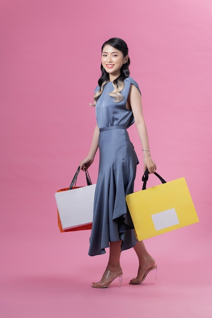 Привлекательная улыбающаяся вьетнамская женщина на высоких каблуках и в синем платье, идущая с бумажными пакетами