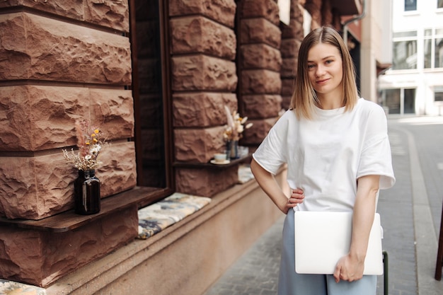 Photo attractive smiling woman in the city with laptop look at camera