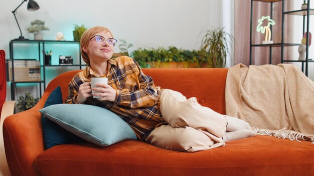 attractive smiling young woman drinking a cup of coffee or herbal tea relaxing resting at home couch