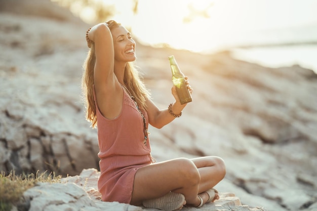 海沿いのビーチパーティーで楽しんでビールを飲みながら魅力的な笑顔の若い女性。