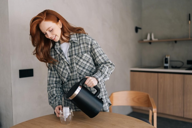 Photo attractive smiling young woman making coffee with drip coffee bag in glass transparent cup standing