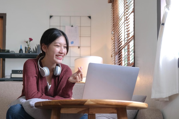 Attractive smiling young woman video call by laptop on sofa at home lifestyle concept