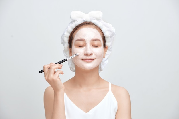 Attractive spa woman applying facial clay mask isolated on white background.