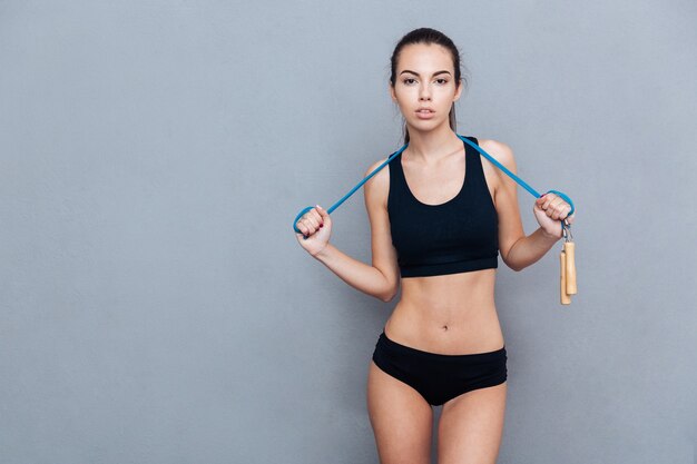 Attractive sport girl holding jumping rope and looking at camera isolated on grey background