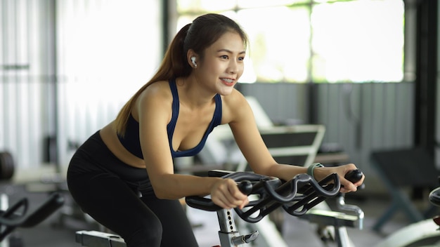 魅力的なスポーツの女性は、フィットネスジムの自転車のトレッドミルマシンで運動します。健康的な活動の概念。