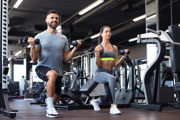 Attractive sports people are working out with dumbbells at gym.