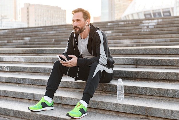 Attractive sportsman in earphones using mobile phone