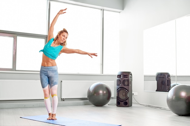 Attractive sportswoman doing exercises on the floor in the modern palates studio Beautiful sportive girl limbering-up and stretching her legs and arms