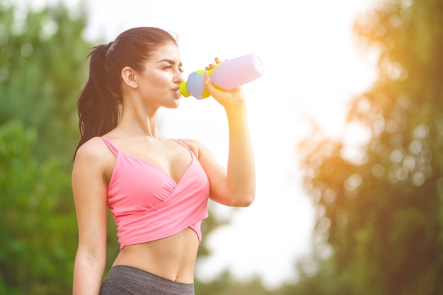 The attractive sportswoman drink a water on the sunlight background