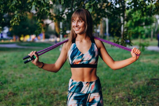 Attractive sporty girl stands with a jump rope and happily smiling outdoor