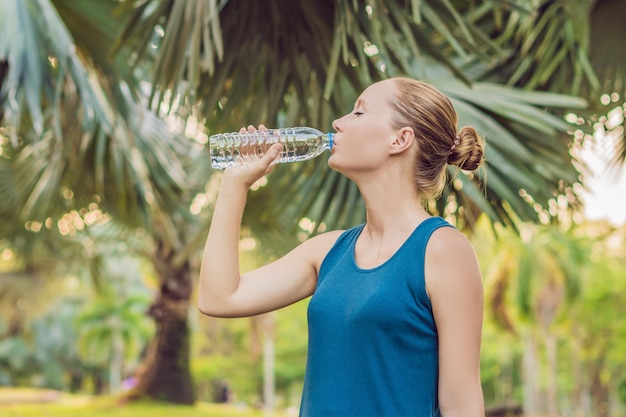 ジョギングやランニングの後にボトルから水を飲む魅力的なスポーティな女性