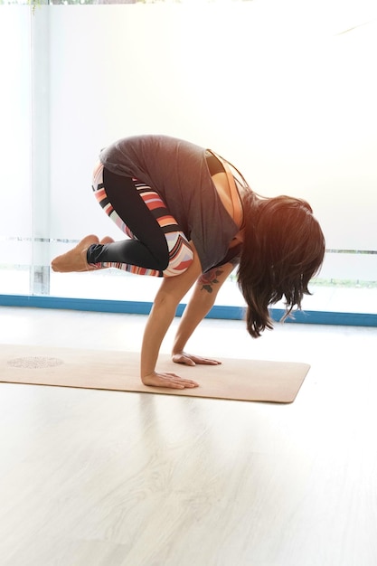 Привлекательная спортивная женщина, практикующая йогу, стоящая в упражнениях с краном, позирует бакасана, тренируясь в тренажерном зале