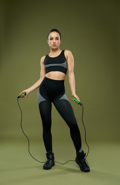 Attractive sporty woman with skipping rope standing in studio