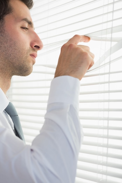 Attractive stern businessman spying through roller blind