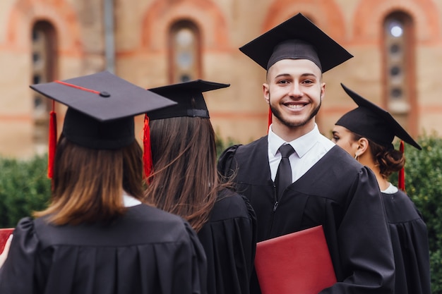 Studente attraente che sta con i suoi amici e che tiene diploma