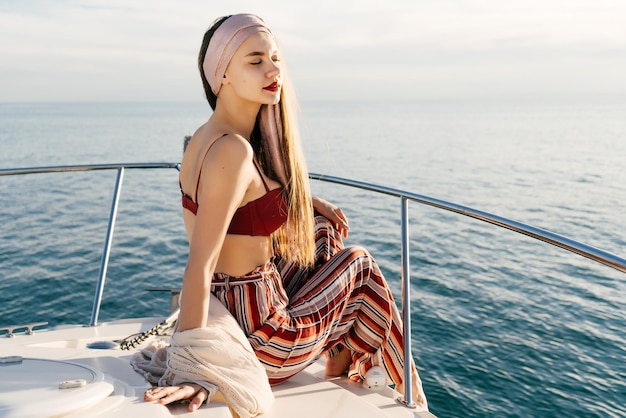 An attractive stylish girl in fashionable pants sits on a boat in the sun relaxes and relaxes