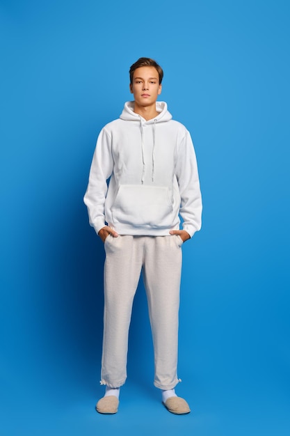 Attractive stylish man wearing white sweatshirt and sweatpants standing over blue studio background