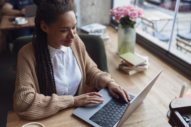 Foto attraente giovane donna afroamericana alla moda che utilizza il computer portatile al caffè