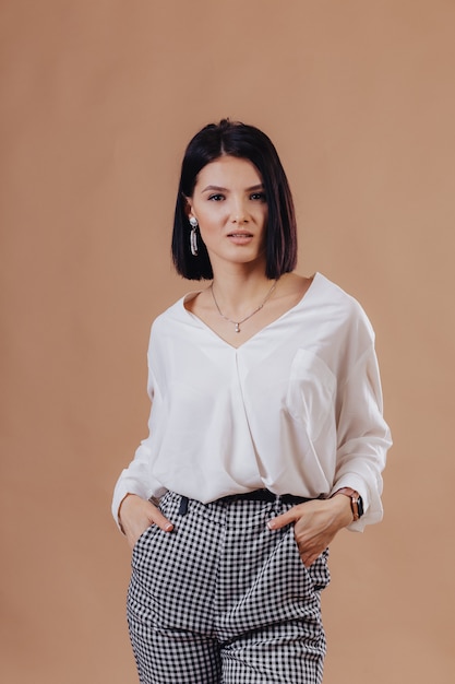 Attractive stylish young girl in business attire posing on cream wall. concept of stylish clothes and sophistication.