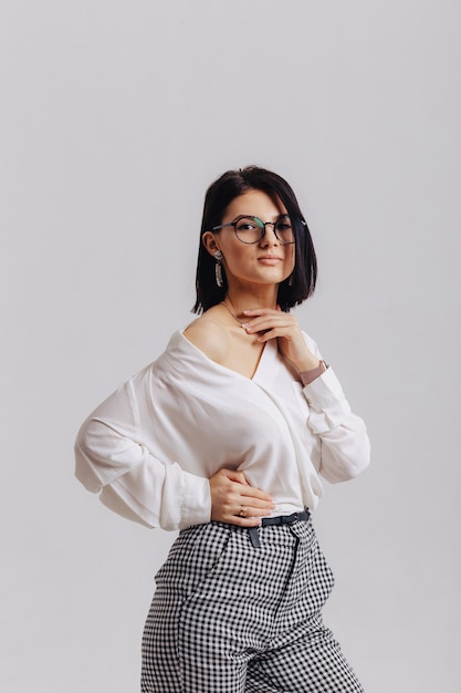 Attractive stylish young girl in business clothes posing on light wall in studio. concept of stylish clothes and sophistication.