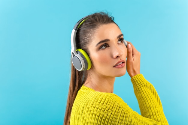 Giovane donna alla moda attraente che ascolta la musica in cuffie senza fili felice che indossa la moda di stile colorato maglione lavorato a maglia giallo isolato sulla parete blu