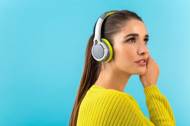 Attraente giovane donna elegante che ascolta musica in cuffie wireless felice indossando un maglione lavorato a maglia giallo in posa di moda in stile