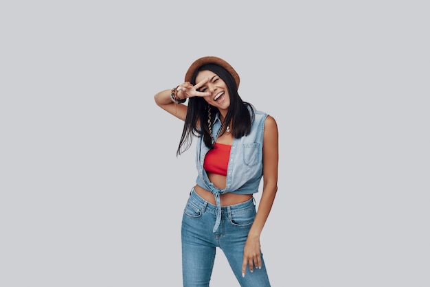 Attractive stylish young woman looking at camera and smiling while standing against grey background