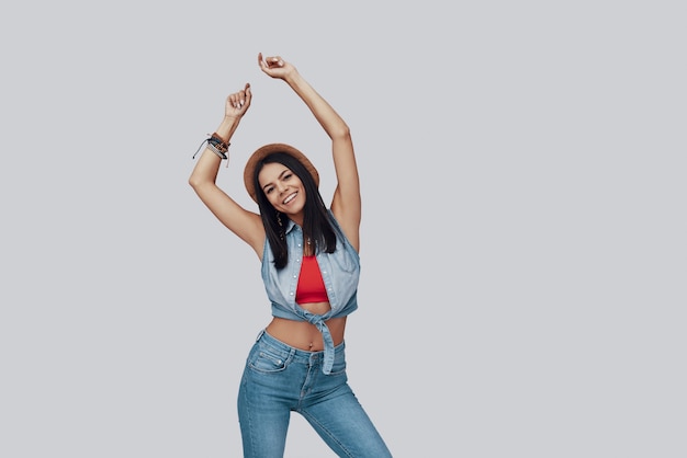 Attractive stylish young woman looking at camera and smiling while standing against grey background