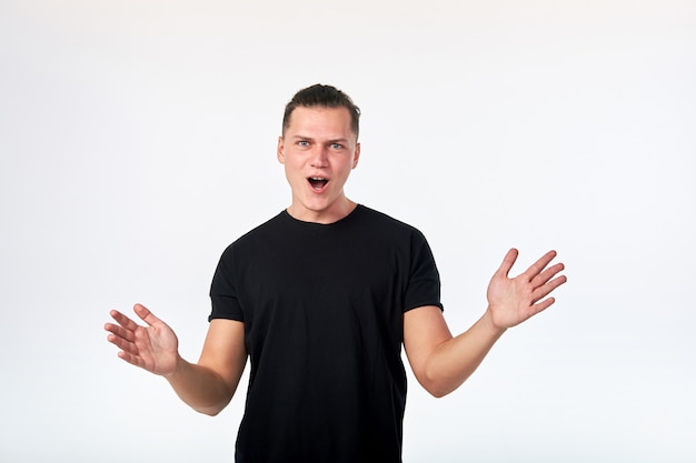 Attractive surprised man standing and looking at camera dressed in black shirt on white background.