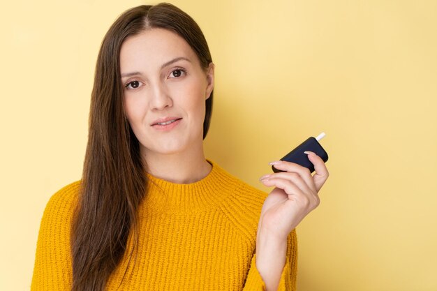 黄色の背景で隔離の笑顔とポーズの電子喫煙デバイスを持つ魅力的なタタール人女性