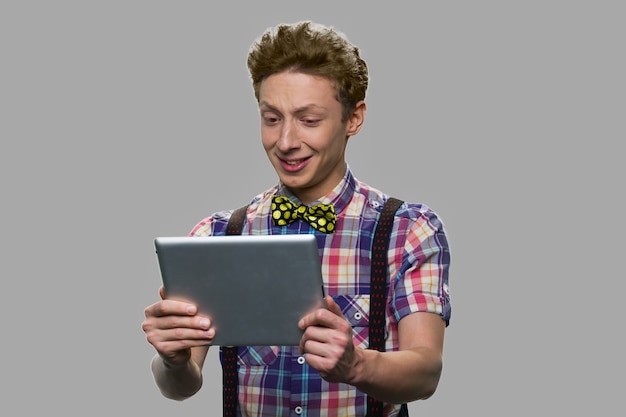 Attractive teen boy having video call. Teenage boy in checkered shirt having video chat using digital tablet against gray background.