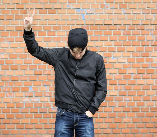Photo attractive teenage boy in urban background portrait of teenage boy showing victory symbol