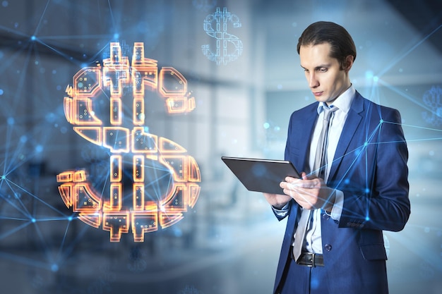 Attractive thoughtful young european businessman with tablet standing in blurry office interior with glowing dollar sign online banking and currency concept double exposure