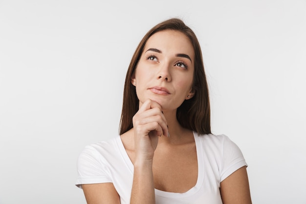 Attractive thoughtful young woman standing isolated over white wall