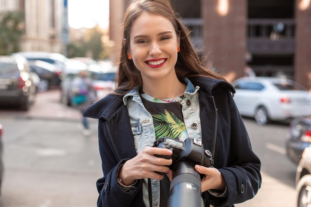 Attractive tourist woman photographer with camera, outdoor in city street. Gorgeous happy caucasian female in casual hipster clothes