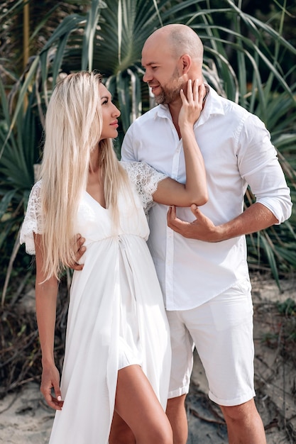 Attractive trendy young couple in white clothes posing together\
against a beach background. beautiful blonde with long hair and a\
bald man are on vacation. phuket. thailand.