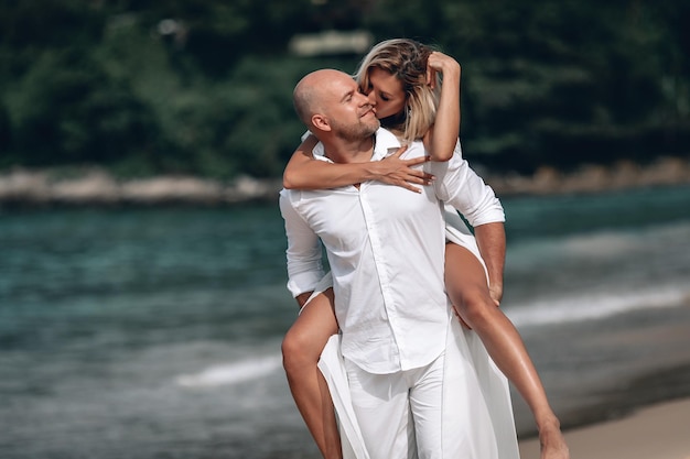 Photo attractive trendy young couple in white clothes  together against a beach background. beautiful blonde with long hair and a bald man are on vacation. phuket. thailand.