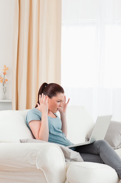 Attractive upset woman gambling with her computer while sitting on a sofa