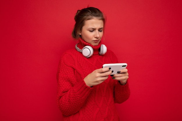 Attractive upset young brunet woman wearing red sweater isolated over red background